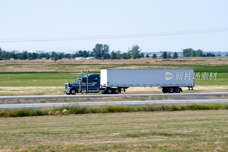 一辆半挂车，牵引着干货车或箱式拖车，沿着非城市分割的高速公路/州际高速公路行驶。